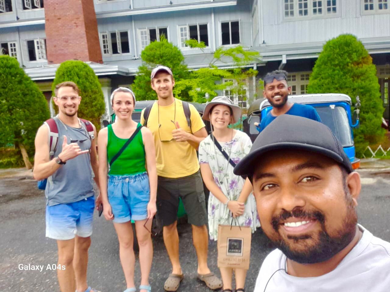 Group of tourists with tuk tuk driver Roshel in front of colonial building in Nuwara Eliya Sri Lanka